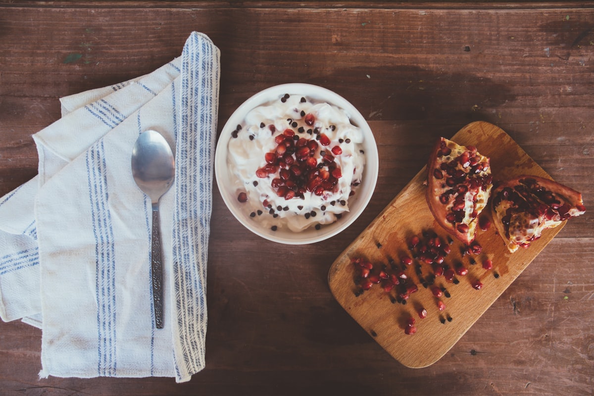 Granaatappel en een schaaltje yoghurt op een houten plank met linnen doek