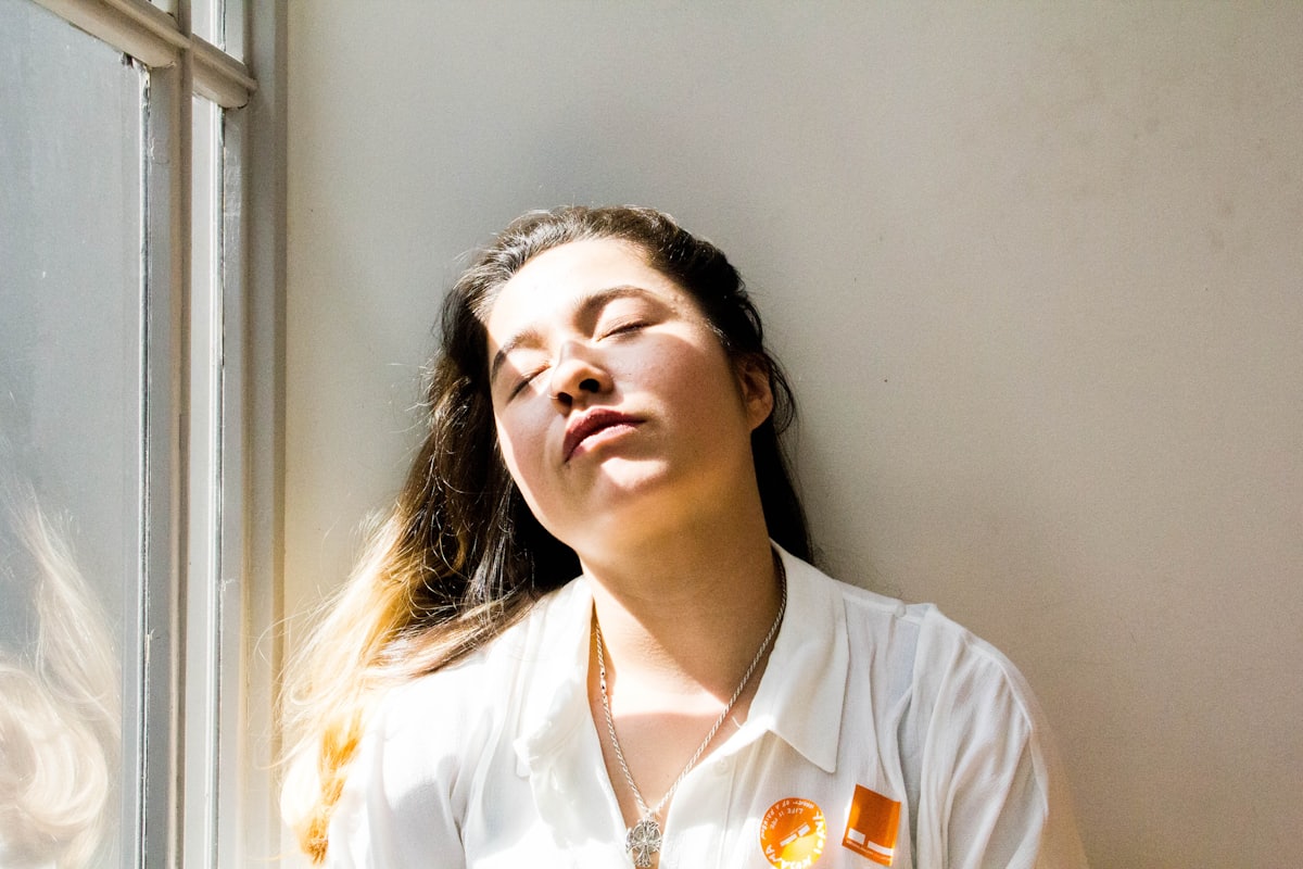 Vrouw die met gesloten ogen uitrust bij een raam in het daglicht